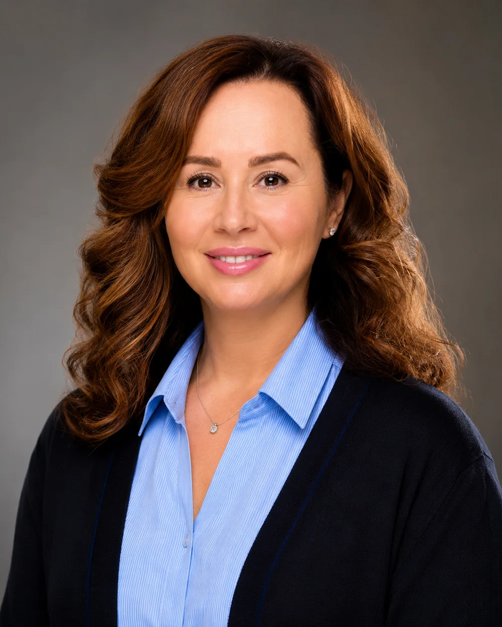 Dr. Alla Patish-Preobrazhenskaya, professional fiduciary, smiling in a navy cardigan over a light blue shirt against a soft gray studio background.